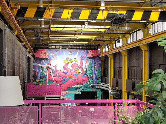 Photo of an industrial space which has been overtaken by an outbreak of pink, including a mural covering an entire wall which features a huge (friendly) pink octopus. People are riding on the octopus tentacles, but it's all very wholesome and not at all what you might be thinking when you read the words "tentacle monster"